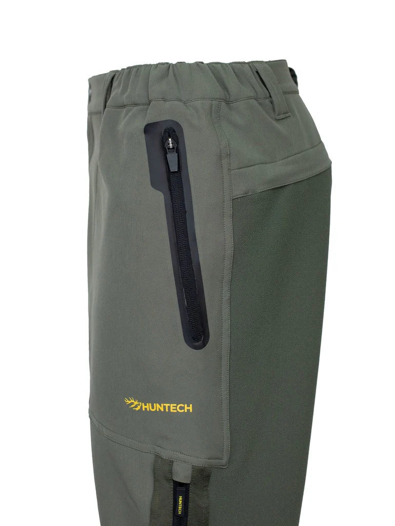 Close up of side zippered pocket on men's three season hunting pants with Huntech logo in bright yellow at the bottom of the pocket. Pants are shown in olive.