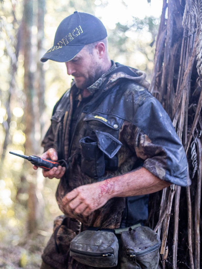 Image of hunter talking on radio, wearing a untech branded, hard-wearing, 330 gsm dual-grid fleece coats with a 500D coated Oxford nylon back overlay and shaped half sleeves that repel light showers. Huntech logo in yellow is on the left breast, with twin chest pockets and a molle GPS pouch that straps to left chest pocket. Shown in kakariki, this coat ships from Australia.