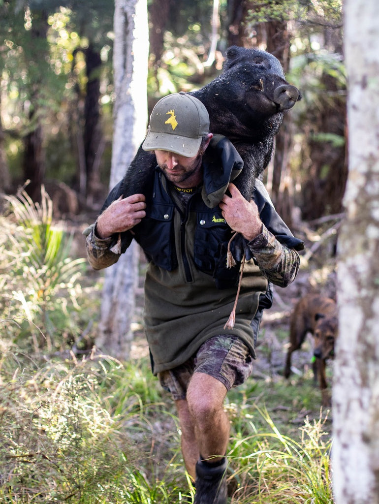 Image of pig hunter with boar slung over his shoulders. He's wearing a Huntech branded, hard-wearing, 330 gsm dual-grid fleece coats with a 500D coated Oxford nylon back overlay and shaped half sleeves that repel light showers. Huntech logo in yellow is on the left breast, with twin chest pockets and a molle GPS pouch that straps to left chest pocket. Shown in military green, this coat ships from Australia.


