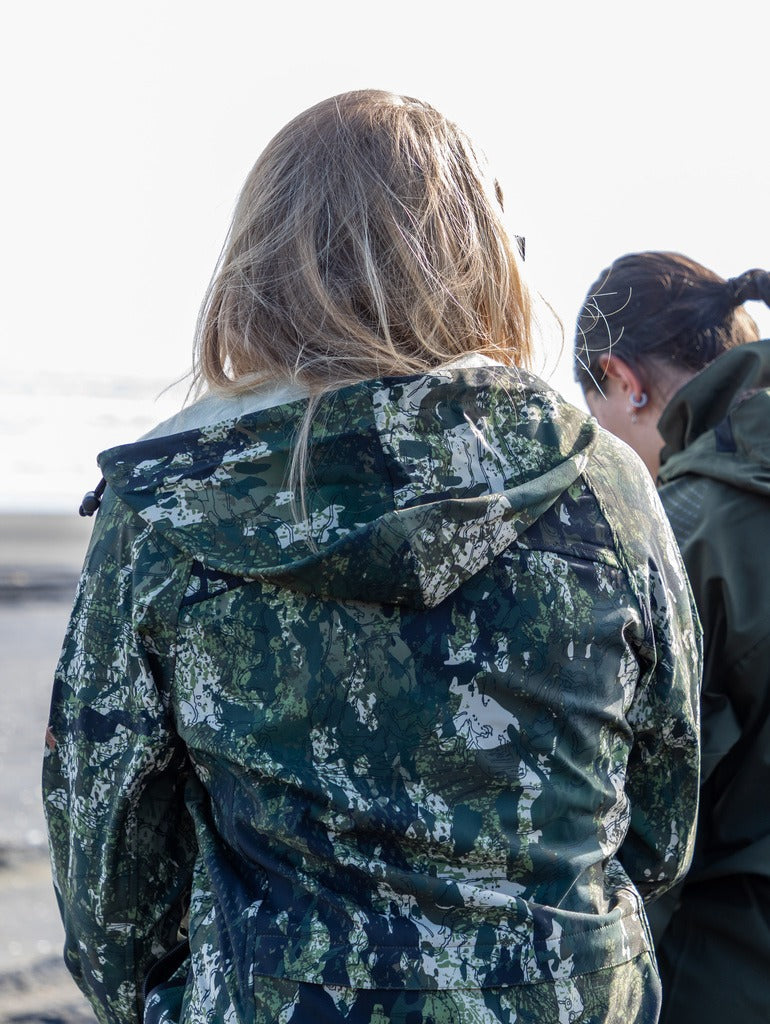 Image of woman taken from behind showing her wearing the trail jacket in the kakariki camo pattern with the hood down.
