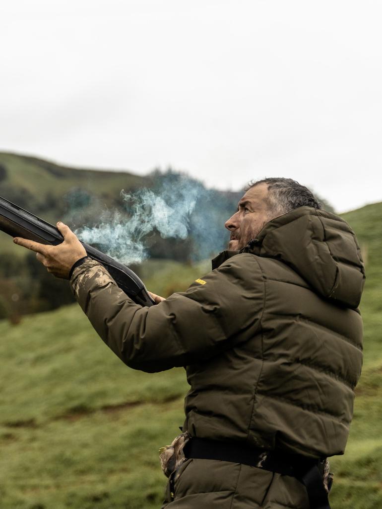 Image of hunter holding a recently fired gun. He's wearing the Olaf puffer jacket in military green.