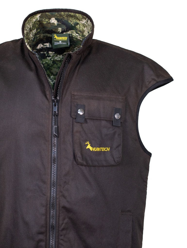 Close up of chest pocket with the Huntech logo in bright yellow and a dome closure, and a high tapered turtleneck. Designed with added shoulder width and collar height it’s offers protection when hauling out an animal on your back. Top of the side pocket is just visible. Shown with kakariki camo lining, this vest ships from Australia.